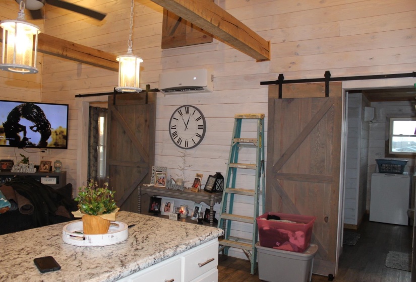 Kitchen with a barn door, wood walls, a wall unit AC, dark wood-style flooring, and white cabinets
