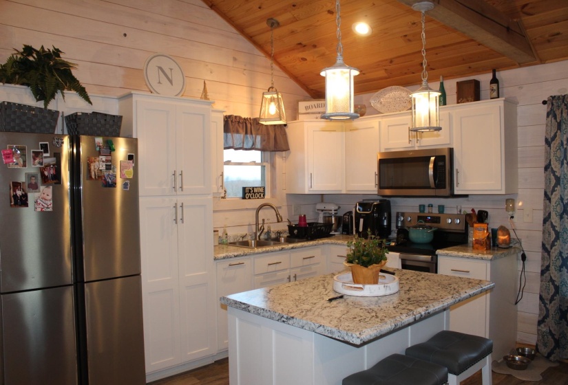 Kitchen featuring appliances with stainless steel finishes, wood ceiling, vaulted ceiling, white cabinets, and wooden walls