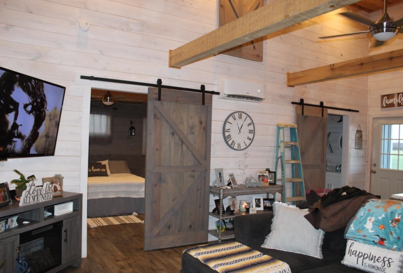 Living room with a barn door, wood walls, a wall mounted AC, wood finished floors, and ceiling fan