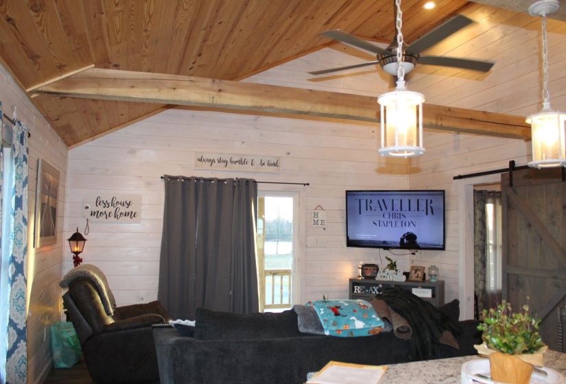 Living room featuring wooden ceiling, a barn door, wooden walls, and a ceiling fan