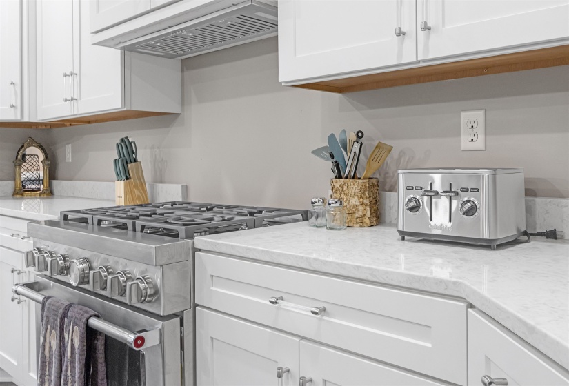 Kitchen with white cabinets, light stone counters, exhaust hood, and stainless steel stove