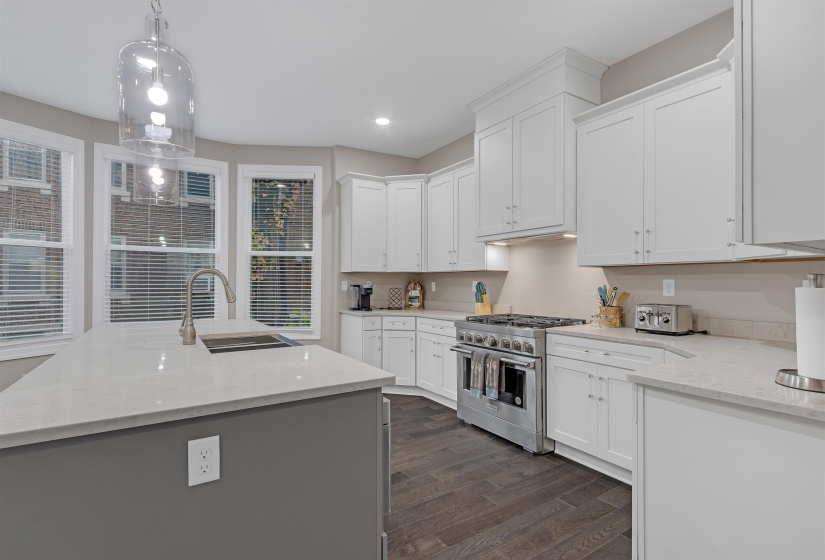 Kitchen with sink, stainless steel stove, dark hardwood / wood-style floors, pendant lighting, and white cabinets