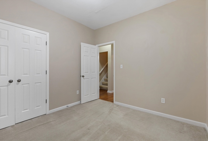 Neutral-toned room featuring light-colored carpeting, a single white entry door with a dark knob, and a pair of white bifold closet doors with dark knobs