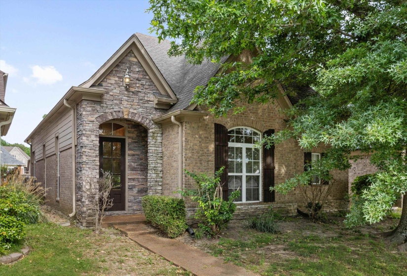 Exterior facade with a stone archway entryway, brick siding, dark wood shutters, and an arched window