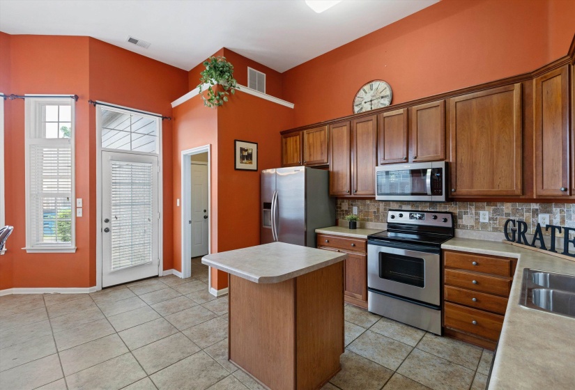 Kitchen featuring wood cabinetry, stainless steel appliances, a tile backsplash, and a central island