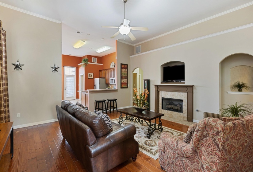 Living area featuring wood-finish flooring, crown molding, a ceiling fan, and an arched fireplace with a tiled surround