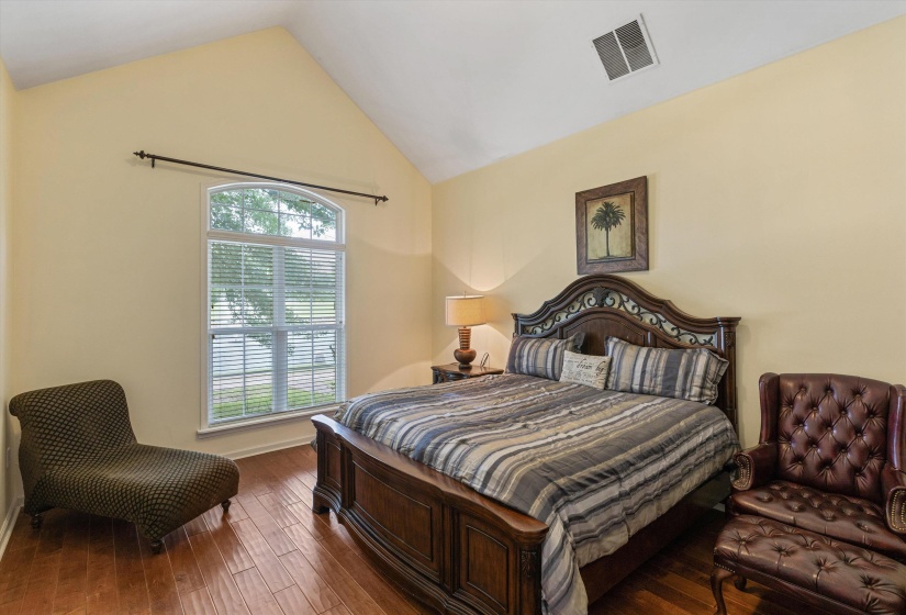 Vaulted ceiling bedroom featuring wood-finish flooring and an arched window with blinds
