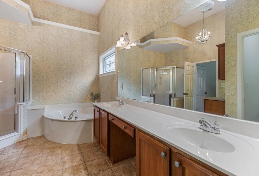 Double vanity with white countertops and integrated sinks, wood-finish cabinetry, a corner soaking tub, and a separate glass-enclosed shower