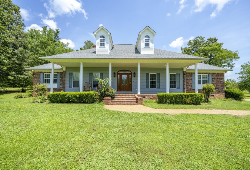 Traditional-style residence featuring a full-width front porch with white columns, light blue siding, and brick accents