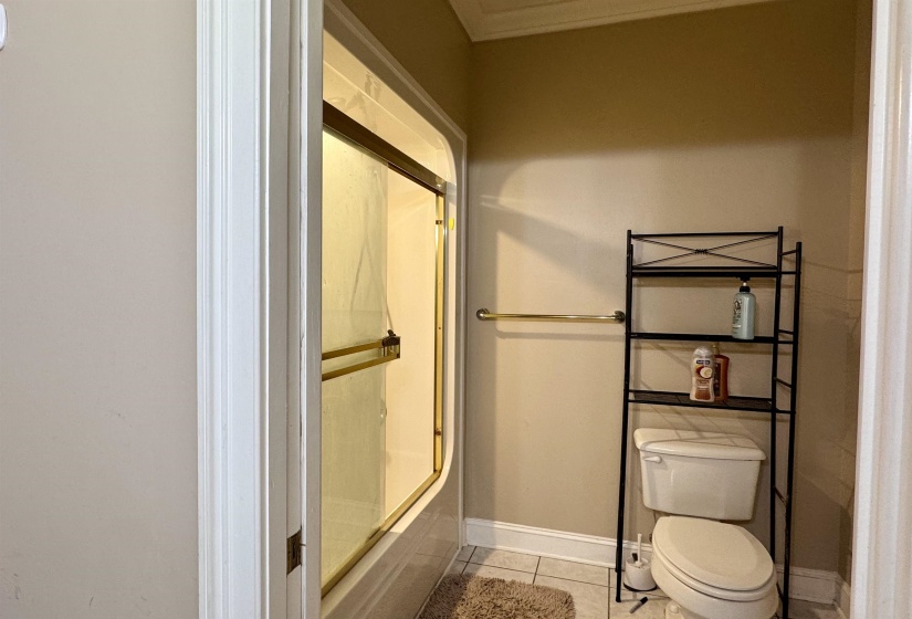 Full bathroom featuring a shower-tub combination with brass-framed sliding glass doors, white tile flooring, and a towel bar