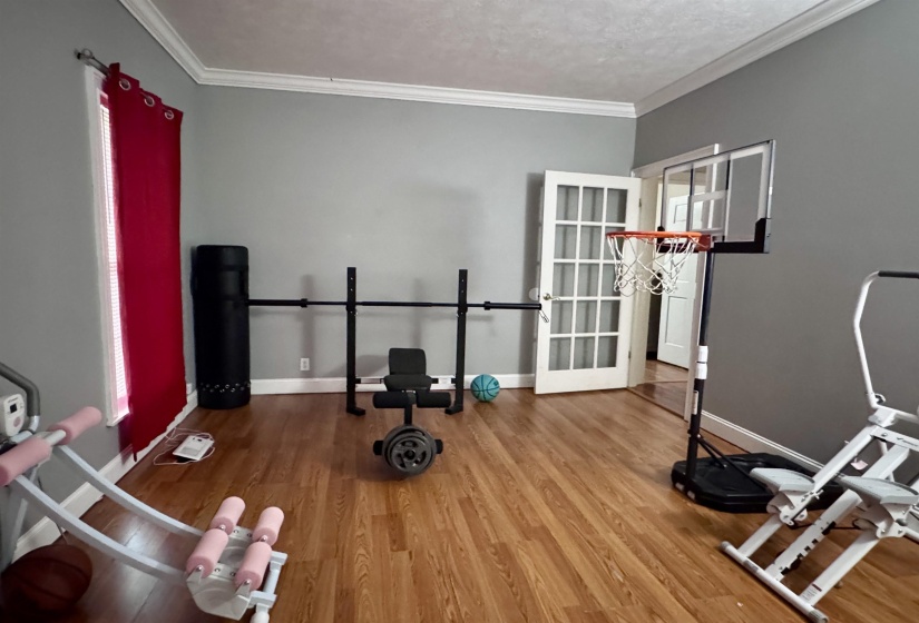 Spacious interior room featuring wood-finish flooring, crown molding, and neutral gray walls