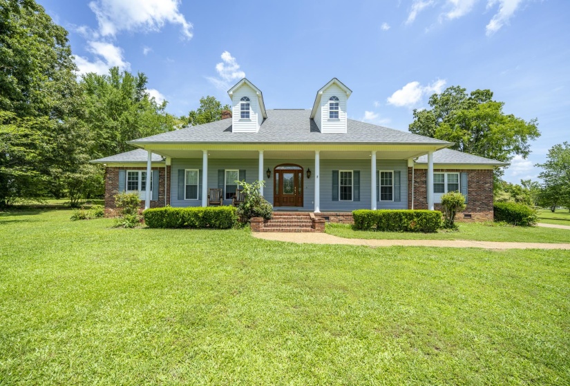 Traditional-style home featuring a full-width covered porch with white columns, light blue siding, and brick accents