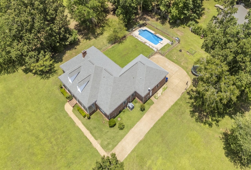 Expansive property featuring a single-story brick residence with a gray shingle roof, a rectangular swimming pool, and a gravel driveway