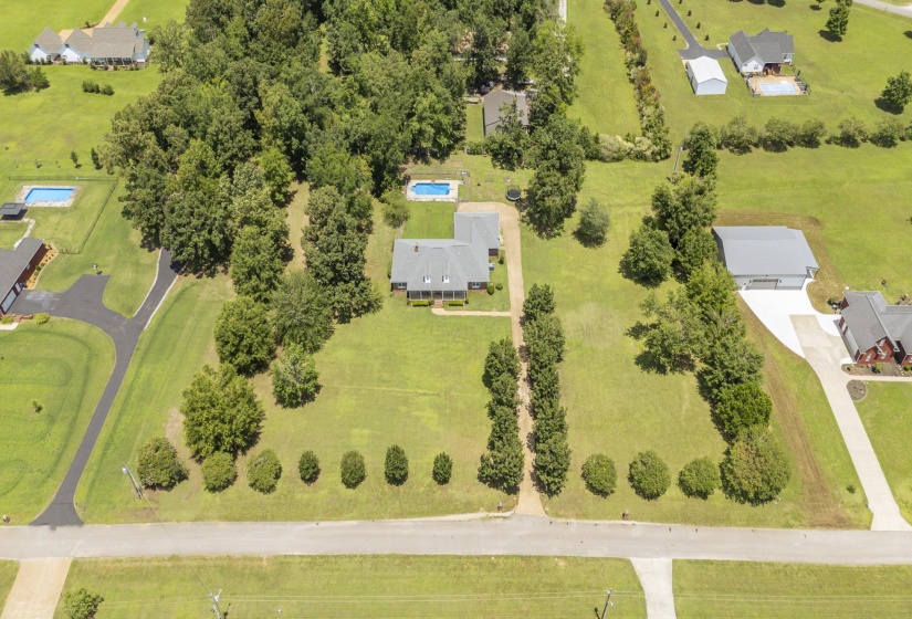 Expansive property featuring a classic two-story residence with a gabled roof, a separate detached garage structure, lush green lawns, mature trees, and a private swimming pool