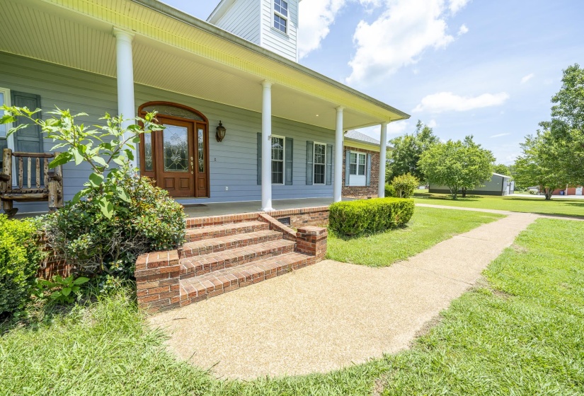 Front entry featuring a wood-panel door with decorative glass, brick steps, and a covered porch supported by white columns