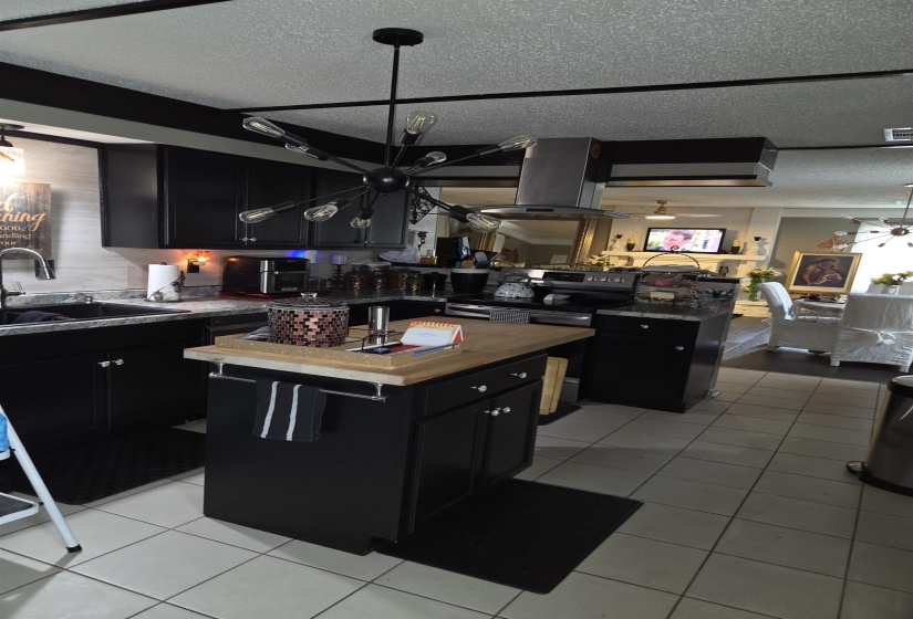 Kitchen featuring black cabinetry, a central island with a wood-finish countertop, stainless steel appliances, and a modern sputnik chandelier