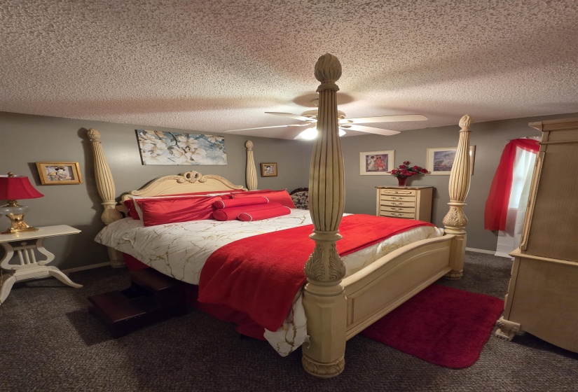 Bedroom featuring a four-poster bed frame, neutral-toned walls, textured ceiling, and a ceiling fan with integrated lighting