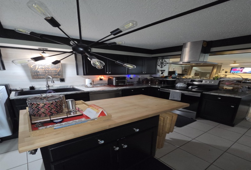 Modern kitchen featuring a Sputnik-style chandelier, black cabinetry, and a movable island with a wood-finish countertop