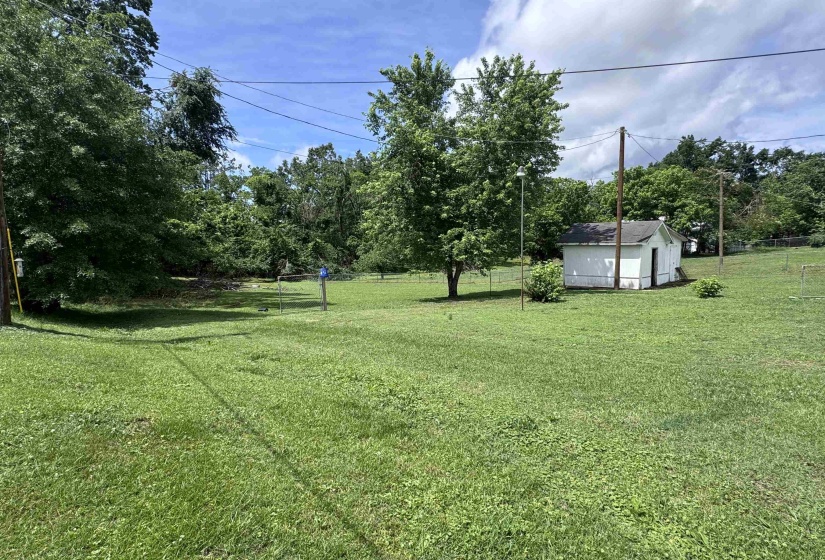 Expansive grassy lot featuring mature trees and a detached outbuilding with white siding