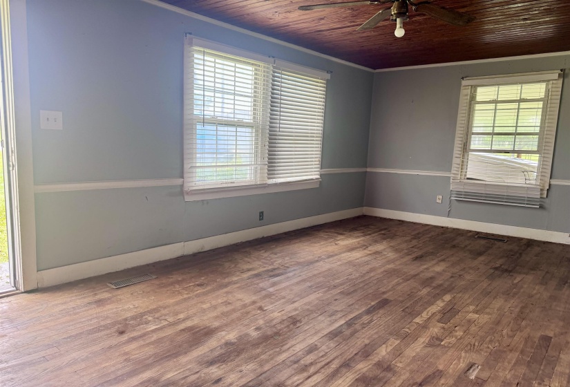 Spacious room featuring wood-finish flooring, two windows with blinds, light blue walls with white trim, and a wood-paneled ceiling with a ceiling fan