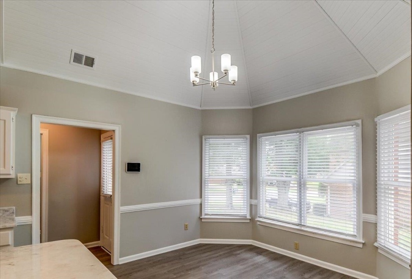 Dining area featuring a vaulted wood-paneled ceiling, a contemporary chandelier, multiple windows with blinds, chair rail molding, and wood-finish flooring