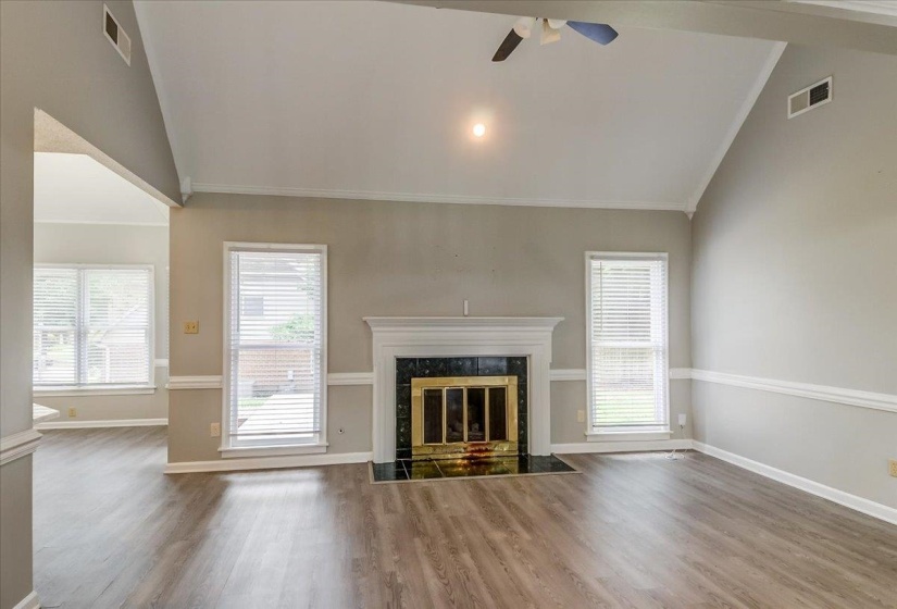 Living area featuring vaulted ceilings, a central fireplace with a dark stone surround and white mantel, and wood-finish flooring