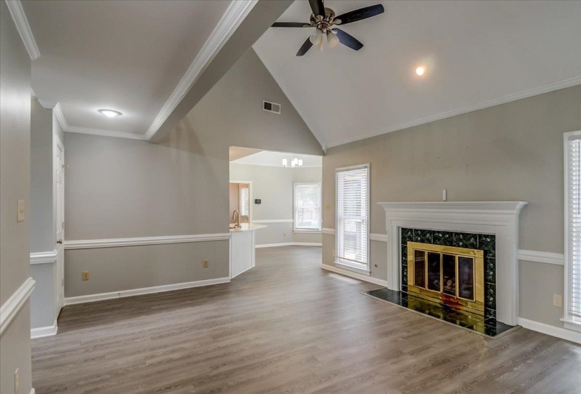 Spacious living area featuring vaulted ceilings, wood-finish flooring, and a white mantel fireplace with a black and green tiled surround
