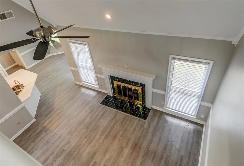 Open-concept living area featuring wood-finish flooring, a contemporary fireplace with a decorative mantel and dark tile surround, and multiple windows