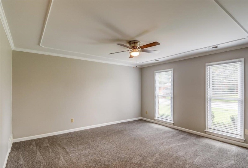 Recessed ceiling with crown molding, ceiling fan, and two windows with blinds