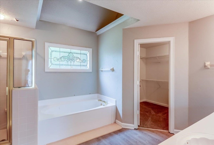 Bathroom featuring a built-in soaking tub, a stained glass-style window, and a glass-enclosed shower with tiled walls