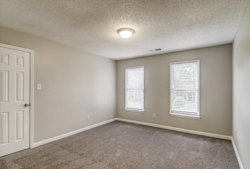 Spacious room featuring neutral tone walls, a textured ceiling, two windows with blinds, a six-panel door, and gray carpeting