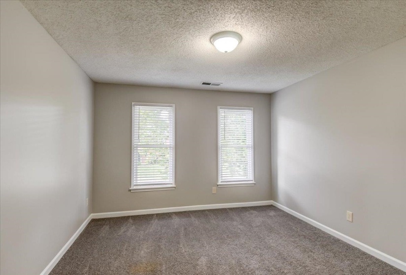Bedroom featuring light neutral wall paint, dark grey carpet, two windows with white blinds, and a flush mount ceiling light fixture