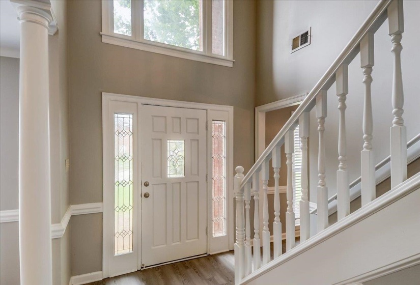 Two-story foyer featuring a white paneled front door with decorative glass inserts, sidelight windows, and a transom window above