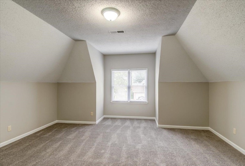 Carpeted room with sloped ceilings and a window featuring blinds