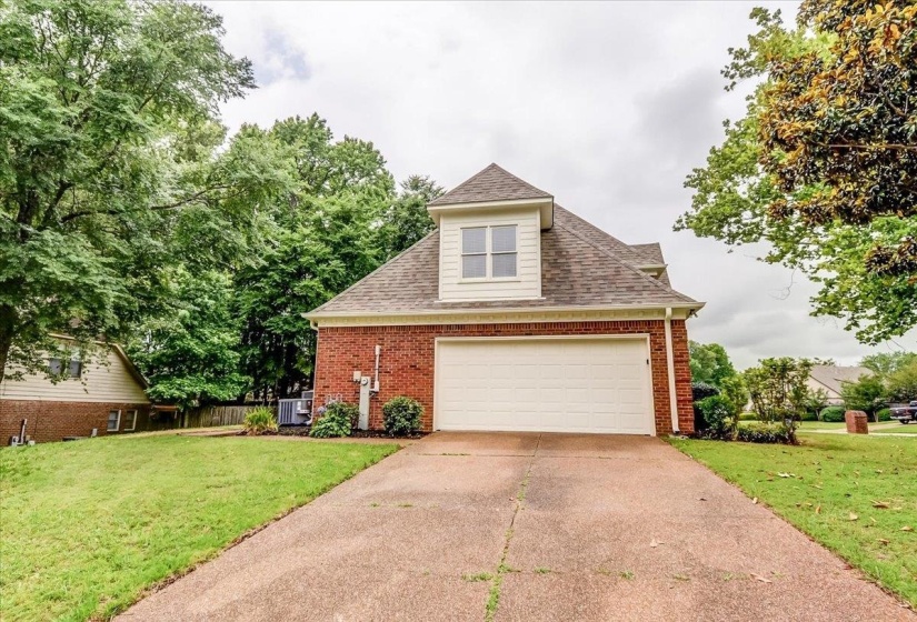 Brick and siding exterior with an attached garage, dormer window, and mature trees framing the property