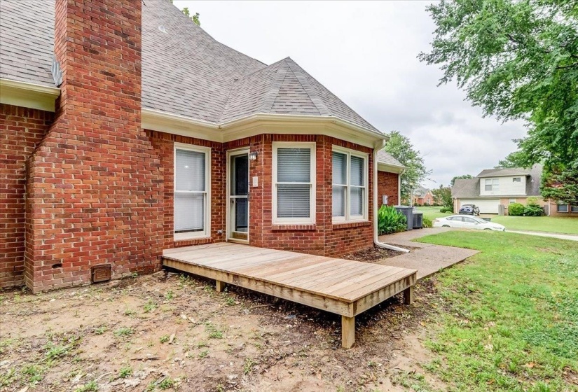 Exterior brick facade featuring a wood deck, multiple windows, a rear entry door, and a chimney structure