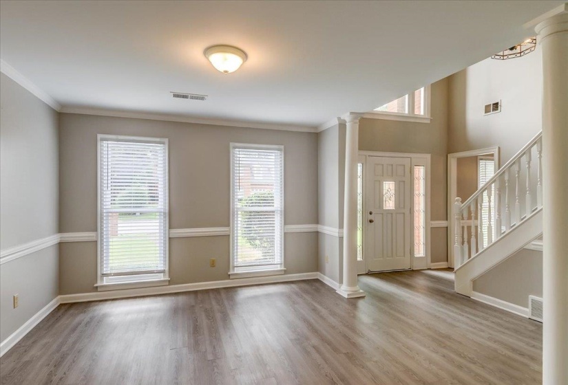 Two-story foyer featuring an ornate front entry door with sidelights, a grand staircase with white balusters, and a decorative column