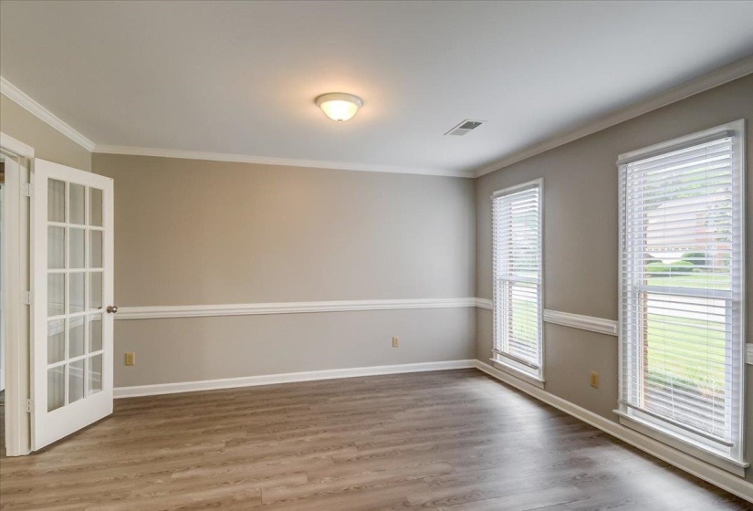 Spacious room featuring wood-finish flooring, neutral-toned walls with chair rail molding, and crown molding