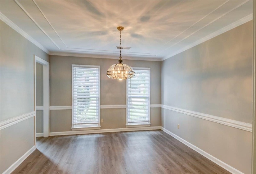 Tray ceiling featuring a central chandelier, wood-finish flooring, two windows with blinds, and decorative wall molding