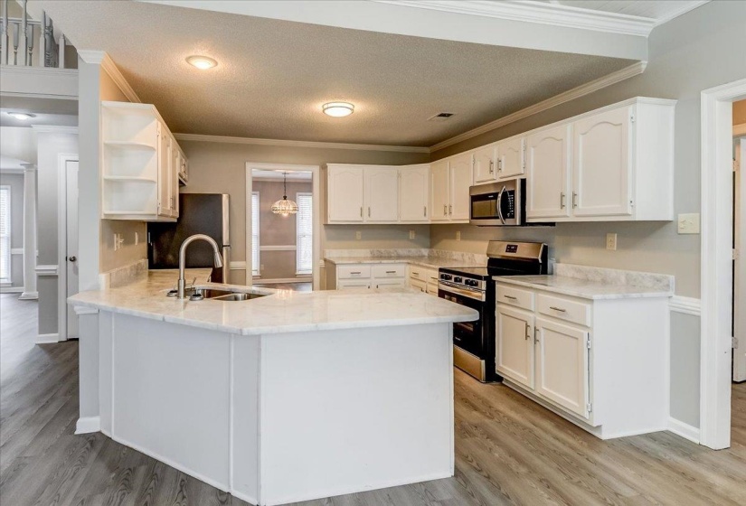 Kitchen featuring white cabinetry, light-toned countertops, a stainless steel sink with gooseneck faucet, a built-in microwave, and wood-finish flooring