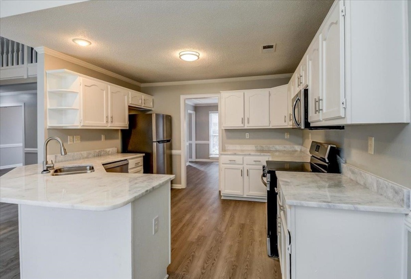 Kitchen featuring white cabinetry, light-toned countertops, stainless steel appliances, and wood-finish flooring