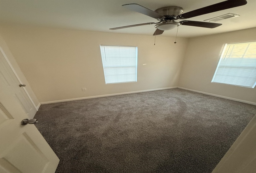 Neutral-toned room featuring a ceiling fan with light fixture, two windows with blinds, and wall-to-wall carpeting