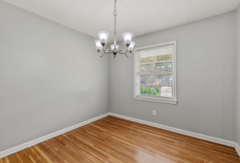 Room with light gray walls, wood-finish flooring, a white trim baseboard, a window with white blinds, and a five-light chandelier