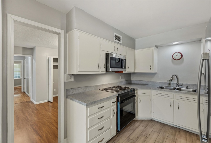 The kitchen features white cabinetry with dark hardware, a stainless steel microwave, and a gas range