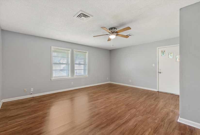 Spacious room featuring wood-finish flooring, light grey painted walls, and a ceiling fan with light fixture