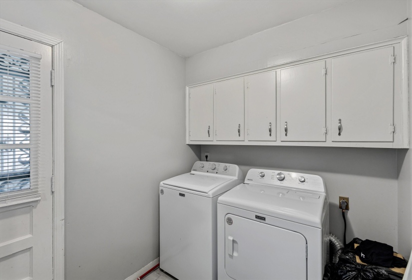 Dedicated laundry area featuring overhead white cabinetry with silver-tone hardware, a louvered door, and light-toned walls