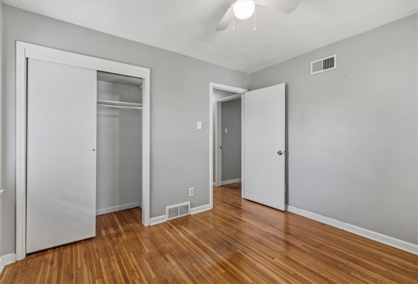 Hardwood flooring throughout featuring light gray walls, a ceiling fan, and a double-door closet with internal shelving