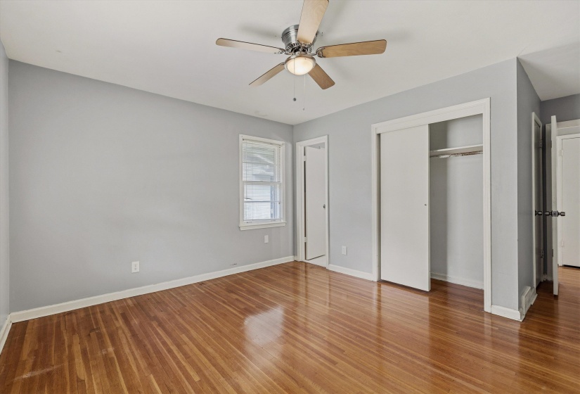 Wood-finish flooring throughout, featuring a ceiling fan with integrated lighting, a window with white trim, and a closet with sliding doors