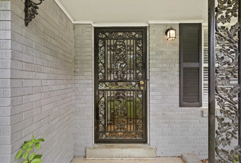 Ornate iron security door with intricate scrollwork, complemented by light gray painted brick siding