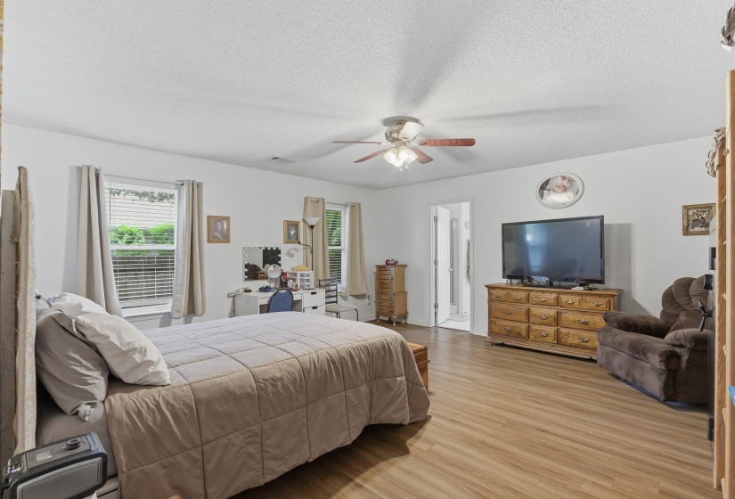 Spacious interior room featuring wood-finish flooring, two windows with blinds, a ceiling fan, and white walls